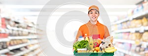 Hygienic smiling Asian delivery man carrying grocery tray box in supermarket banner photo