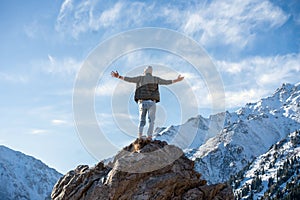 Hyped man standing on a rock surrounded by snowy mountains and sky