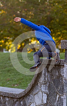 A hyperactive kid is jumping off a high wall as he is running away.