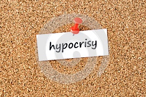 Hypocrisy. Word written on a piece of paper, cork board background