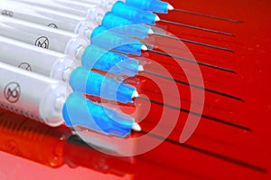 Hypodermic syringe. Syringes with blue needles on a red background. Medical Injectors.
