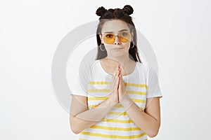 I beg you help me out. Troubled serious and gloomy girlfriend in stylish outfit and sunglasses, holding hands in pray