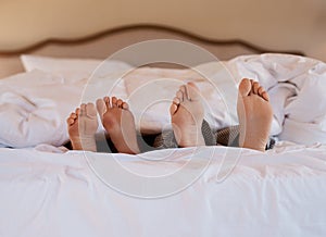 I belong next to you. Shot of an unrecognizable couples feet poking out under the sheets while lying in bed.