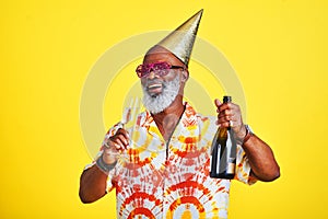 I came here to party. a funky and cheerful senior man celebrating and drinking champagne in studio against a yellow