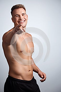 I can help you get muscles like mine. Studio portrait of a muscular young man pointing to the camera against a grey