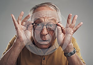 I can see clearly now. Studio shot of an elderly man adjusting his spectacles against a grey background.