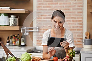 I can store thousands of recipes on my tablet. Portrait of an attractive young woman using her tablet in the kitchen.