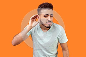 I can`t hear you! Portrait of nosy brunette man trying to hear gossip. studio shot  on orange background