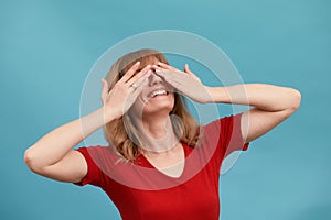 I can't see you. Portrait of pretty woman closing her eyes with two palms, blue studio background