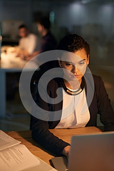 I cant believe Im working overtime again. a young businesswoman using her laptop while working overtime in the office.