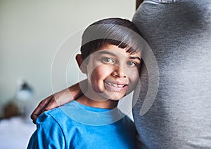 I cant wait to be a big brother. Cropped portrait of an adorable little boy standing against his mothers pregnant belly.