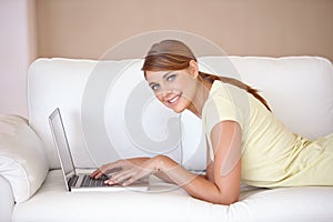 I couldnt be more content. Portrait of an attractive young woman using her laptop while relaxing on a sofa at home.
