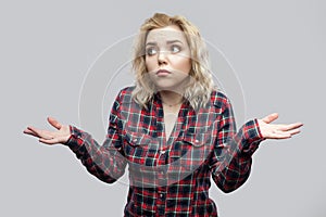 I don`t know. Portrait of confused beautiful blonde young woman in casual red checkered shirt standing with raised arms and