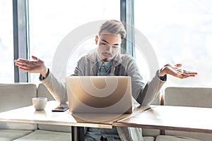 I don`t know!Portrait of confused handsome bearded young freelancer in grey blazer are sitting in cafe and making video call on