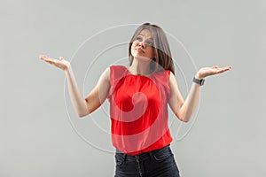 I don`t know! Portrait of puzzled beautiful brunette young woman in red shirt standing with raised arms, looking away thinking an