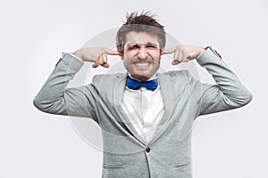 I don`t want to hear. Portrait of worried handsome bearded man in casual grey suit, blue bow tie standing with closed eyes and