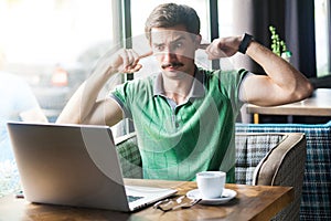 I don`t want to hear you! Young dissatisfied businessman in green t-shirt sitting, looking at laptop screen on video call and