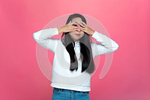 I don't want to see. Pretty cute shy young asian girl covering her eyes by palms no on pink studio background