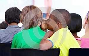 I dont feel like working. A young schoolboy whispering into his friends ear during class.