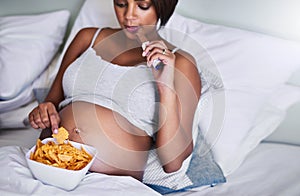 I eat whatever I crave. a pregnant woman enjoying a chocolate and potato chips in bed.