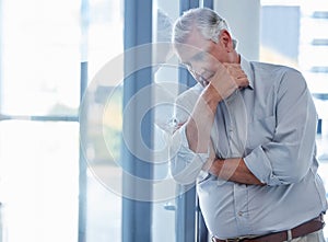 I always fear for the future of my business. a mature businessman looking stressed out while standing at a window in an