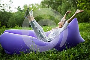 I am free. Pretty young woman lying on inflatable sofa lamzac with reised hands in the air while resting on grass in park