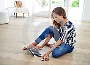 I get more work done at home. Full body shot of an attractive young woman sitting and using a laptop in the living room