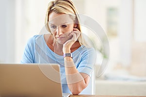 I get more work done when its done from home. an attractive mature woman sitting and using a laptop while in her living