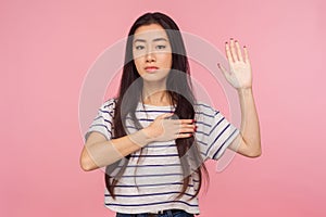 I give you promise! Portrait of responsible, honest girl with brunette hair keeping hand on chest and raising palm