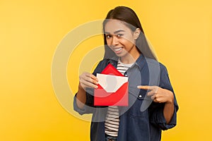 I got love letter on Valentine`s day. Happy beautiful girl in denim shirt pointing letter in red envelope, holding greeting card