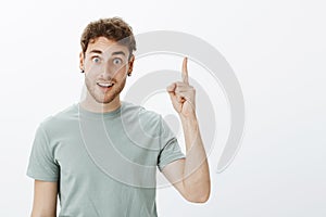I have great idea, listen. Portrait of positive happy european male model with short curly hair, raising index finger in