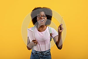 I have idea. Creative black female student raising pencil up and exclaiming eureka on yellow studio background
