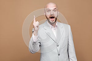 I have idea. Portrait of handsome amazed middle aged bald bearded businessman in classic gray suit standing with finger up and lo