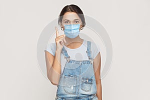 I have idea. Portrait of happy young brunette woman with surgical medical mask in denim overalls standing surprised and looking at