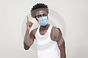 I have Idea. Portrait of young man in white shirt with surgical medical mask standing holding finger up and looking at camera