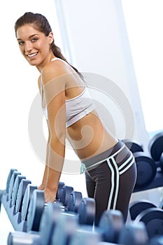 I have more than just inner strength. A gorgeous young woman standing by a rack of dumbbells at the gym.