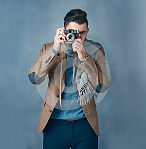 I have my eyes on you. Studio portrait of a stylishly dressed handsome young man holding a vintage camera.