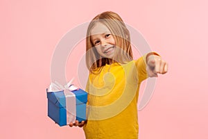 I have present for you! Portrait of kind generous little girl standing with gift box, bonus, pointing finger to camera photo