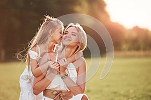 I have secret for you. Mother and daughter enjoying weekend together by walking outdoors in the field. Beautiful nature