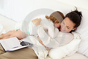 I always have time for you. A young mother lying in bed and giving her toddler a hug with an open notebook lying on her