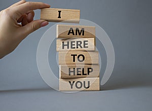 I am here to help symbol. Concept words I am here to help on wooden blocks. Beautiful grey background. Businessman hand.
