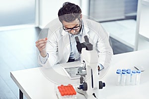 I hope this is the right formula. a focused young male scientist making notes while holding up a test tube inside a