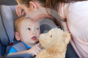 I hope were stopping at the toy store, Mom. a mother kissing her baby boy sitting in a car seat.