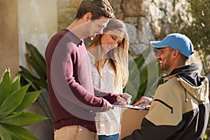 I just need your name right here. a courier delivering a package to a smiling young couple at home.