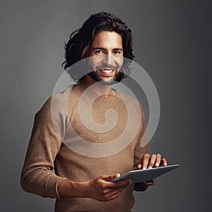 I keep my lifestyle digitized. Studio shot of a handsome young man using a digital tablet against a gray background.