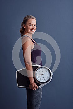 I keep track of my weight. Studio portrait of an attractive mature woman holding a weightscale against a blue background