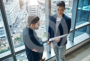 I know youll be able to help me nail this project. two young businessmen discussing paperwork in a modern office.