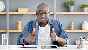 I like distant work. Happy black man gesturing thumbs up sitting at workplace at home office