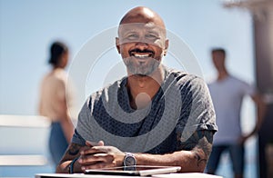 I like to go here all alone. Portrait of a cheerful middle aged man seated at a table outside next a beach promenade.