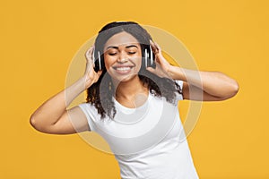 I like this tune. Positive black woman enjoying music with closed eyes, touching wireless headphones and dancing